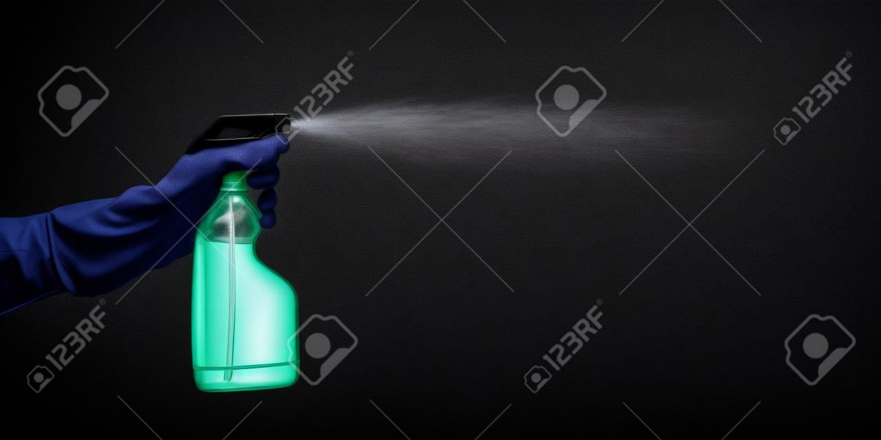 hand with rubber glove holding cleaning bottle and spraying liquid, on black background