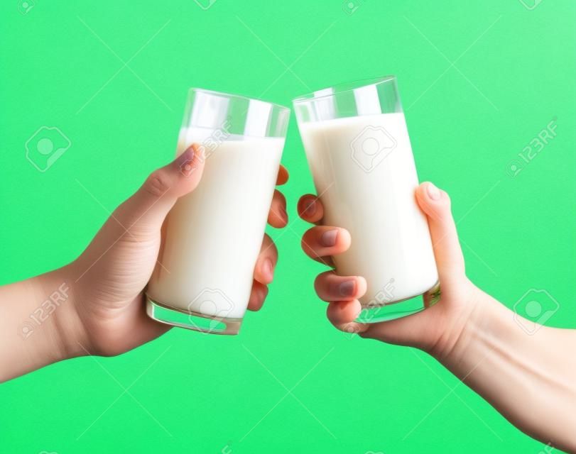 Due mani che tengono bicchiere di latte su fondo verde, bicchieri di latte tintinnanti
