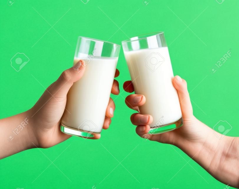 Due mani che tengono bicchiere di latte su fondo verde, bicchieri di latte tintinnanti