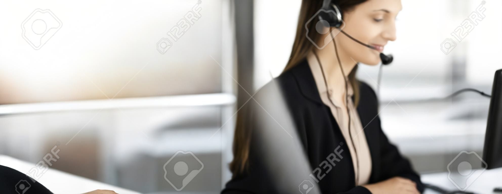 Young man with headsets is talking to a client, while sitting in modern sunny office. Call center operators at work