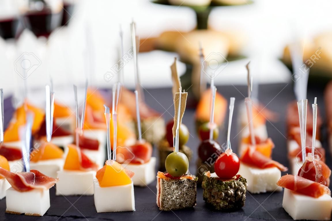 Delicious appetizers and canapes on table at wedding reception in the restaurant. Luxury catering service. Italian delicatessen, prosciutto snacks, cheese and olives. . High quality photo