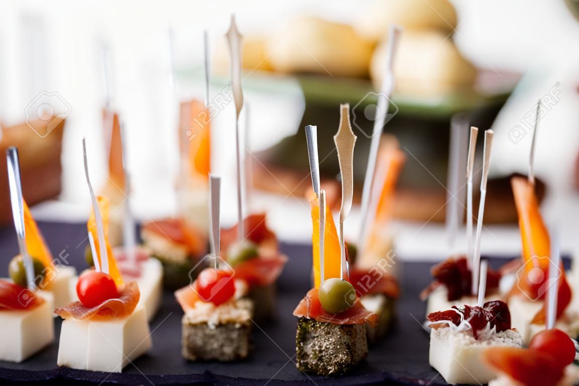 Delicious appetizers and canapes on table at wedding reception in the restaurant. Luxury catering service. Italian delicatessen, prosciutto snacks, cheese and olives. . High quality photo