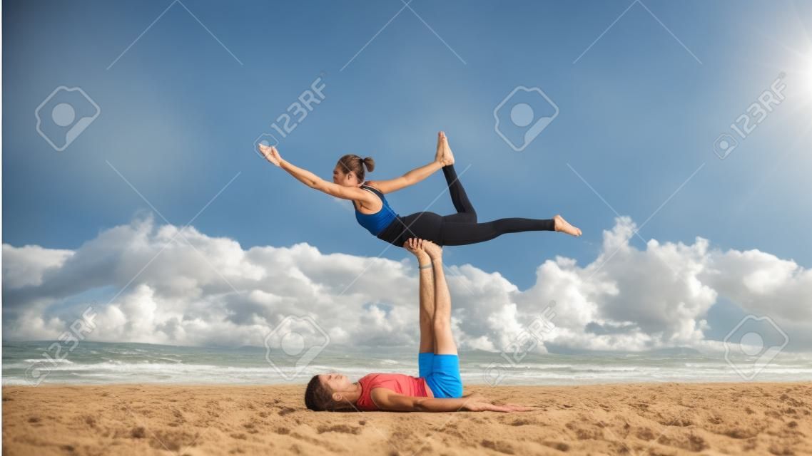 Fit sporty couple practicing acro yoga with partner together on the sandy beach.