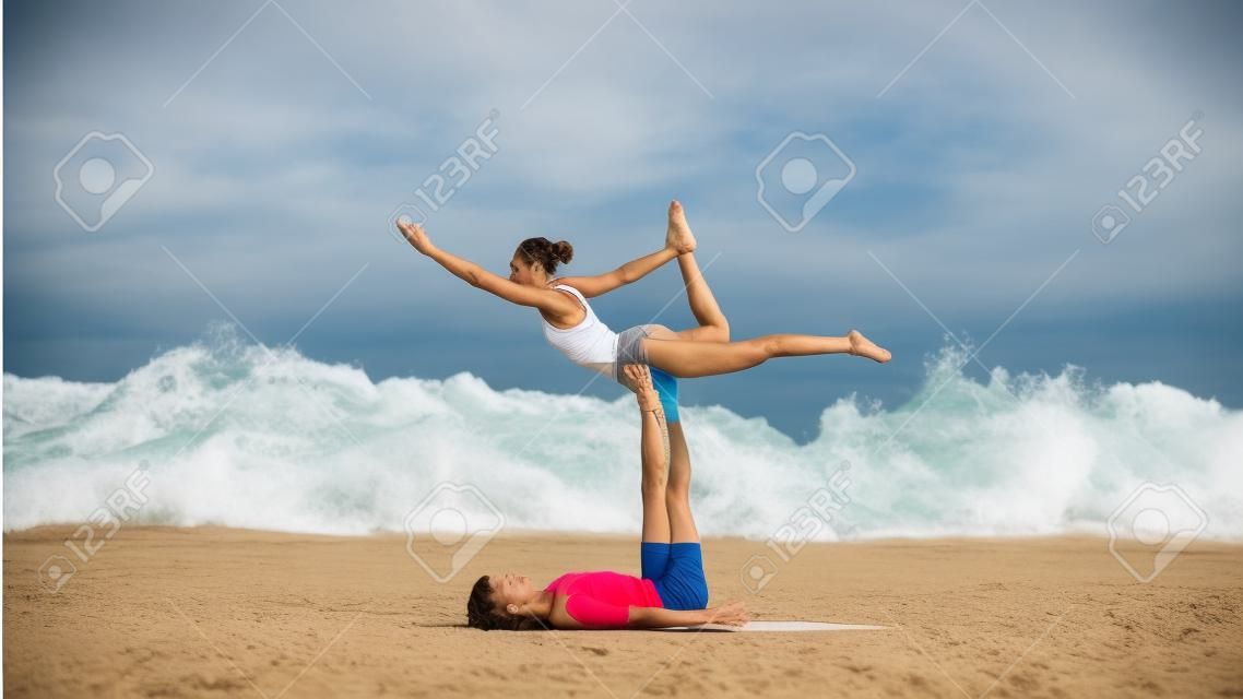 Fit sporty couple practicing acro yoga with partner together on the sandy beach.