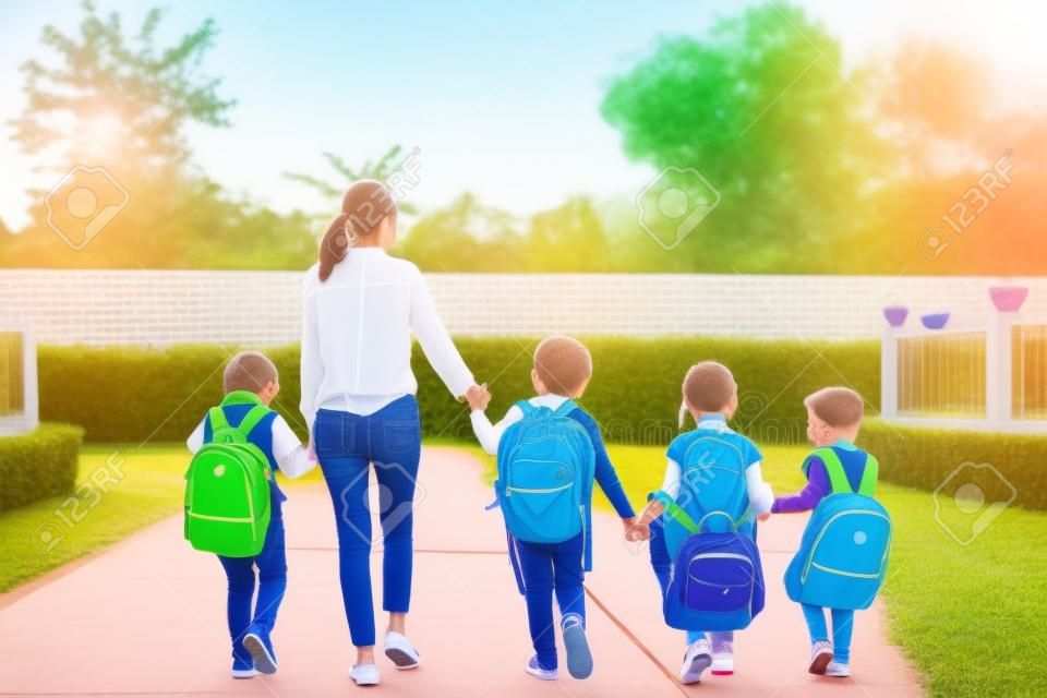 Group of preschool student and teacher holding hands and walking to home. Mom bring her children go to school together. Back to school and Education concept. People and lifestyles theme. Back view