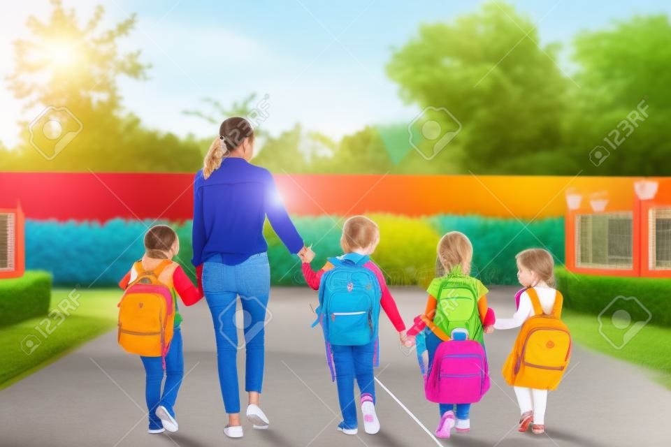 就学前の生徒と教師のグループが手をつないで家まで歩いて行きます。お母さんは子供たちを一緒に学校に連れて行きます。学校と教育の概念に戻ります。人とライフスタイルのテーマ。バックビュー
