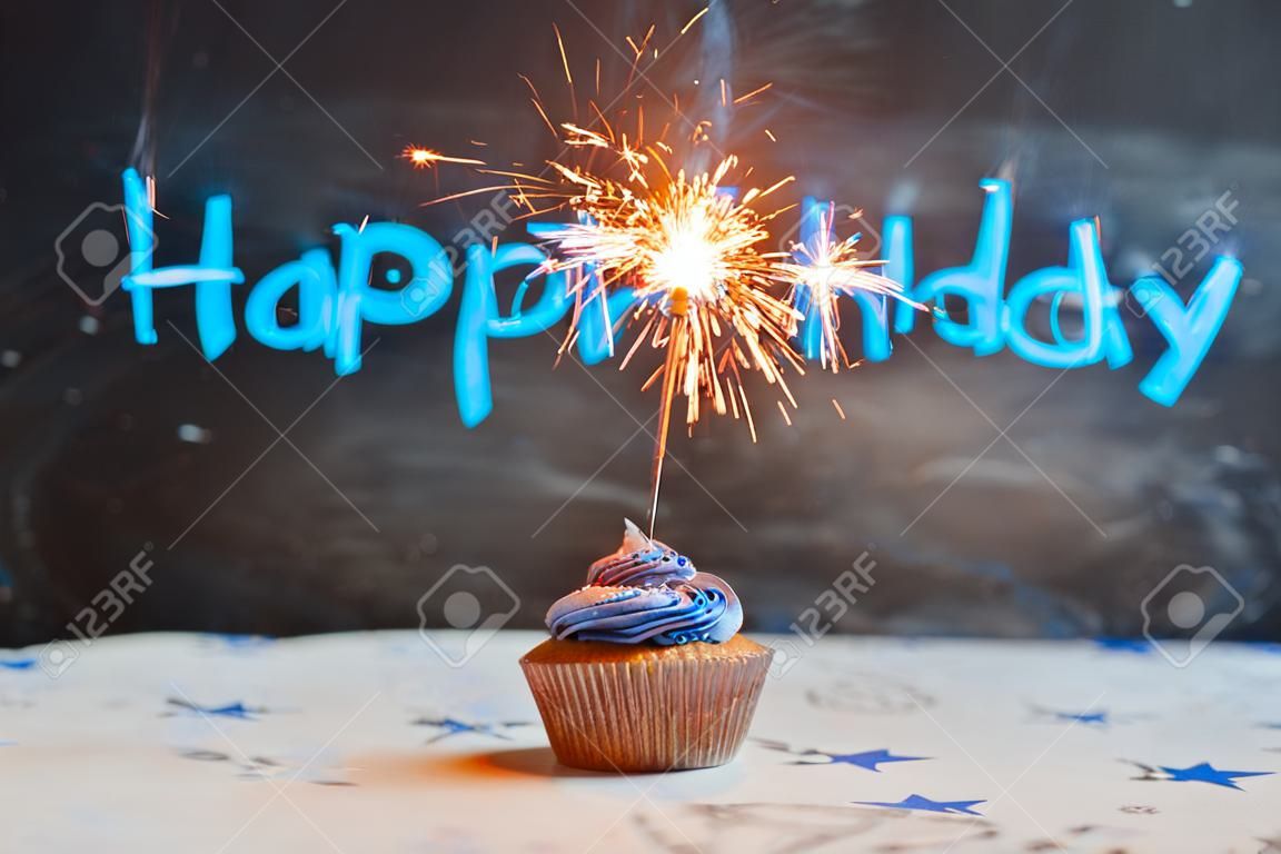 Petit gâteau d'anniversaire avec un sparkler sur un fond bleu.