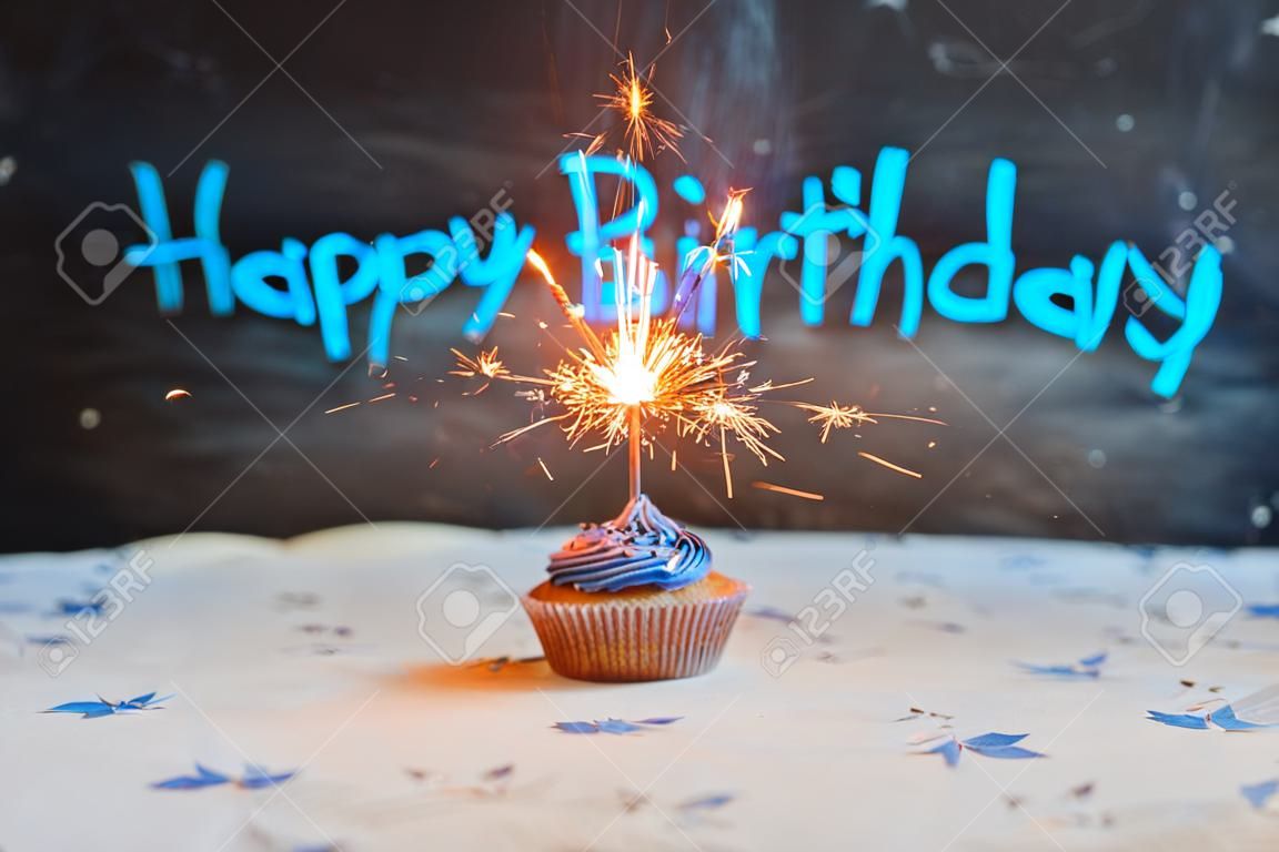 Geburtstags-Kuchen mit einer Wunderkerze über einen blauen Hintergrund.