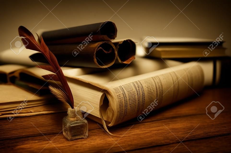 Quill pen y una hoja de papiro enrollada sobre una mesa de madera con libros antiguos