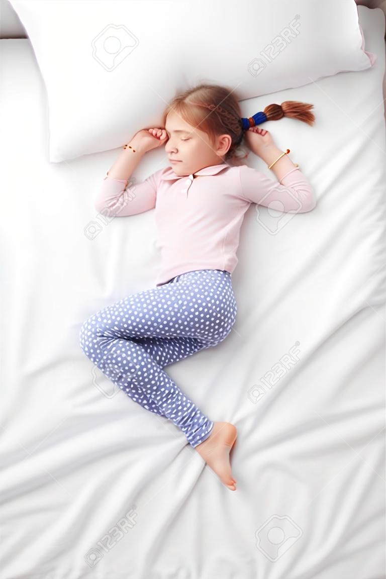 上面白いベッドで寝ているおさげのかわいい少女の写真。寝ているポーズの概念