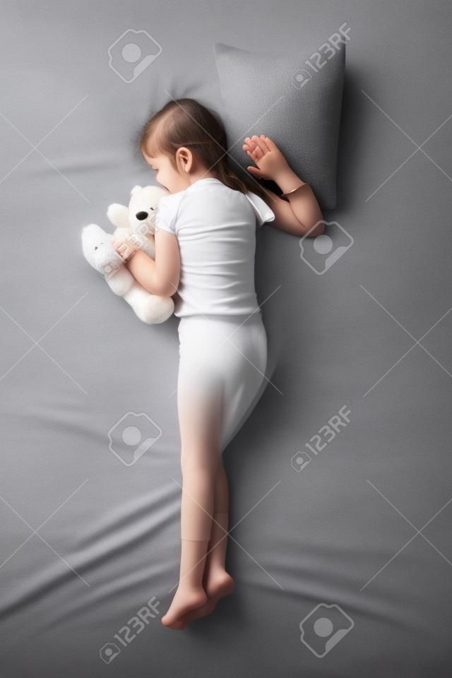 Draufsicht Foto des kleinen netten Mädchens Schlafen auf dem Bauch mit Teddybär. Konzept der schlafenden Posen