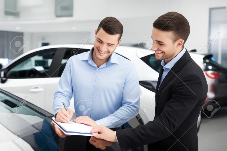 Photo of young male consultant and buyer signing contract for new car in auto show. Concept for car rental