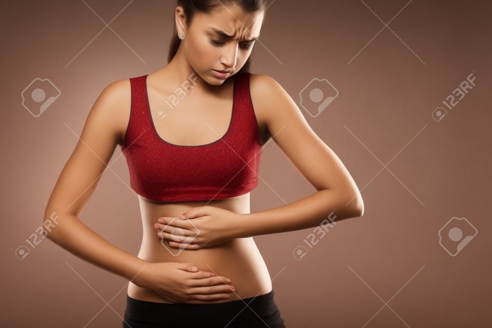 Body pain. Studio shot of beautiful young woman with dark brown hair. Woman suffering from stomach pain. Red spot on stomach
