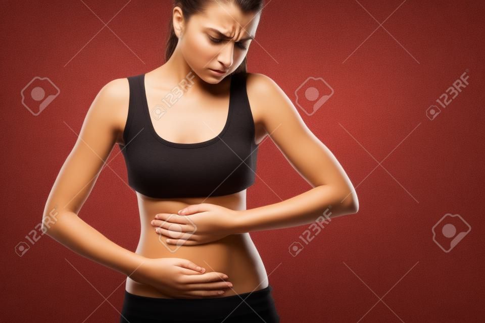 Body pain. Studio shot of beautiful young woman with dark brown hair. Woman suffering from stomach pain. Red spot on stomach