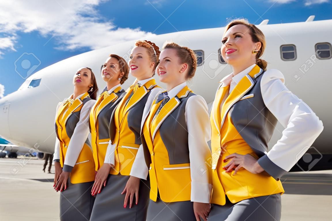 Vrolijke stewardessen in de buurt van vliegtuigen op het vliegveld