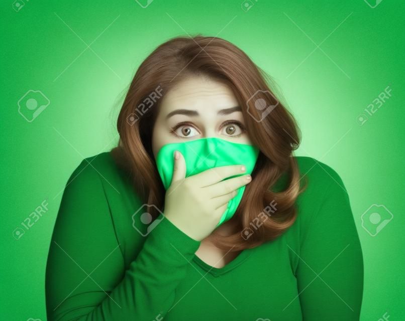 Closeup portrait middle aged shocked young woman, covering her mouth, wide open eyes, isolated green background. Negative human emotion, facial expression, feeling, signs, symbol, reaction