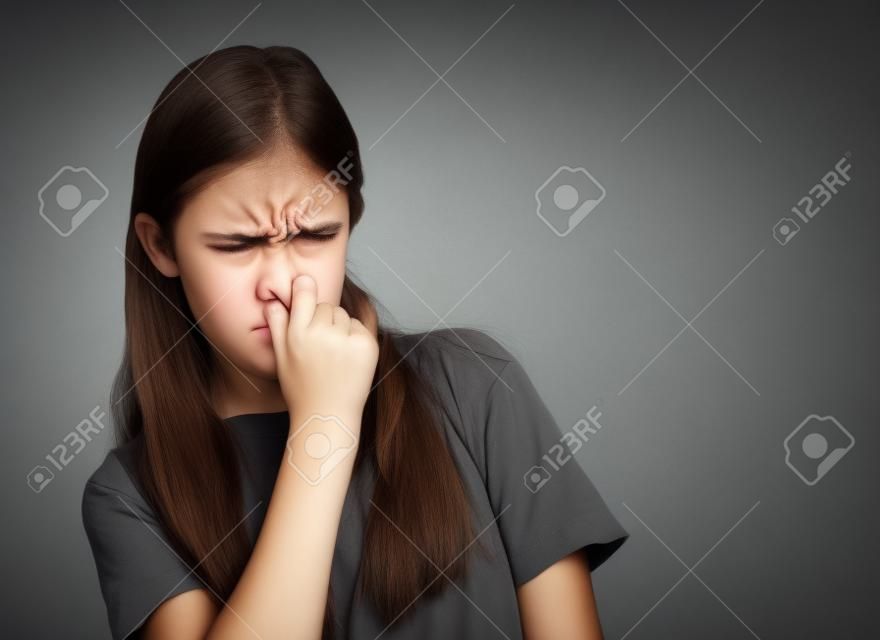 Closeup portrait teenager girl with disgust on face pinches nose, something stinks, very bad smell, situation isolated grey wall background. Negative human emotion facial expression feelings, reaction