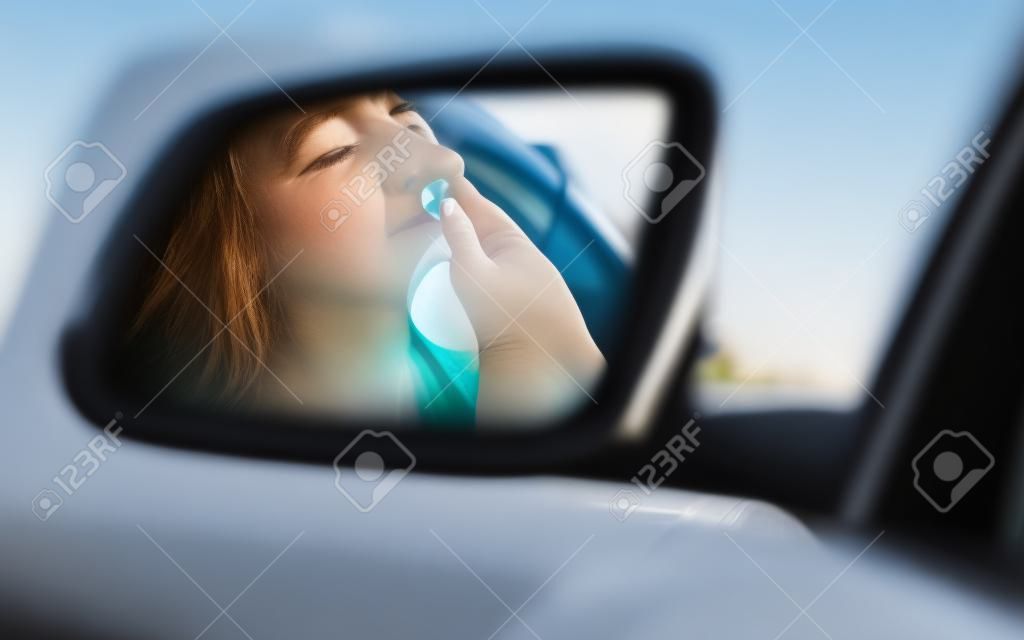 Side view mirror view reflection sleepy tired fatigued yawning exhausted young woman driving her car in traffic after long hour. Transportation sleep deprivation accident concept