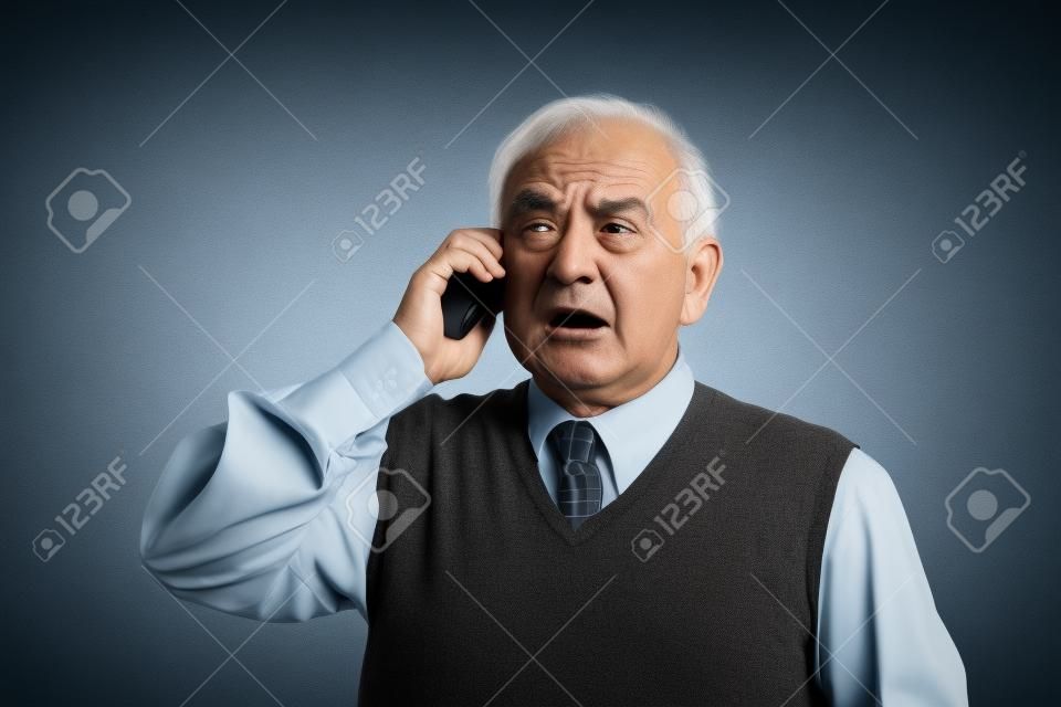 Homem idoso irritado que fala no telefone móvel isolado no fundo da parede cinzenta. emoções negativas