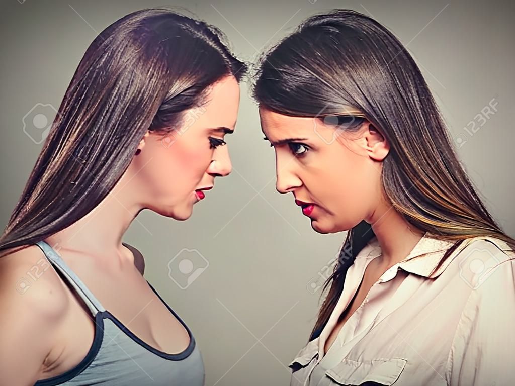 Profil boczny nieszczęśliwych młodych przyjaciół żeński patrząc na siebie head to head stojącej na szarym tle ściany. Trudności Przyjaźń, problemy w koncepcji pracy