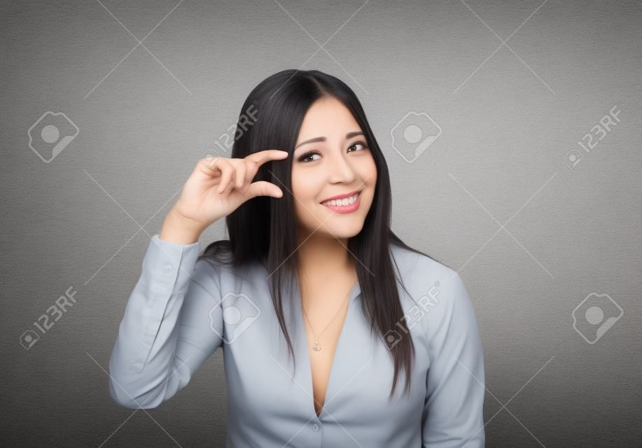Woman showing small amount size gesture with hand fingers isolated on gray wall background. Human emotion facial expression feelings symbol body language