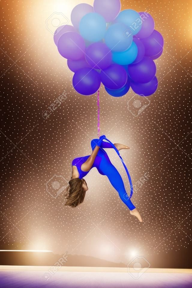 Menina ginasta senta-se em um anel acrobático. Anel segurando balões.