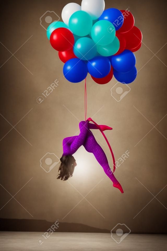 Menina ginasta senta-se em um anel acrobático. Anel segurando balões.