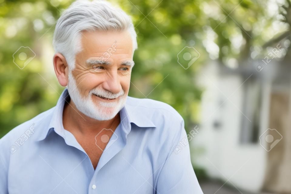 Homem branco mais velho com cabelos grisalhos, vestindo uma camisa, sorrindo e olhando para longe em local ao ar livre com luz natural.