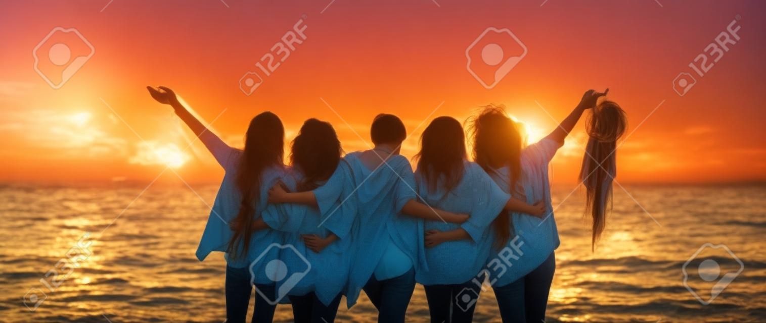 Romance and emotion concept with group of people women friends viewed from back hugging and ejoying the sunset in outdoor nature sea vacation concept - friendship and freedom for travelers