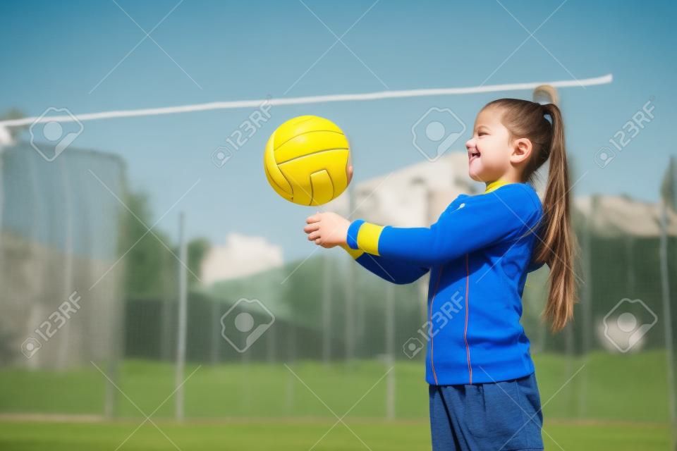 Nettes Mädchen, das Ballmädchen mit einem blauen gelben Volleyball spielt