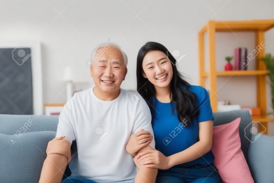 Retrato da filha asiática bonita abraçando e sentar-se com o pai mais velho. Mulher atraente neta visita o homem maduro sênior em casa, aproveite passar o tempo juntos na sala de estar, em seguida, olhando para a câmera