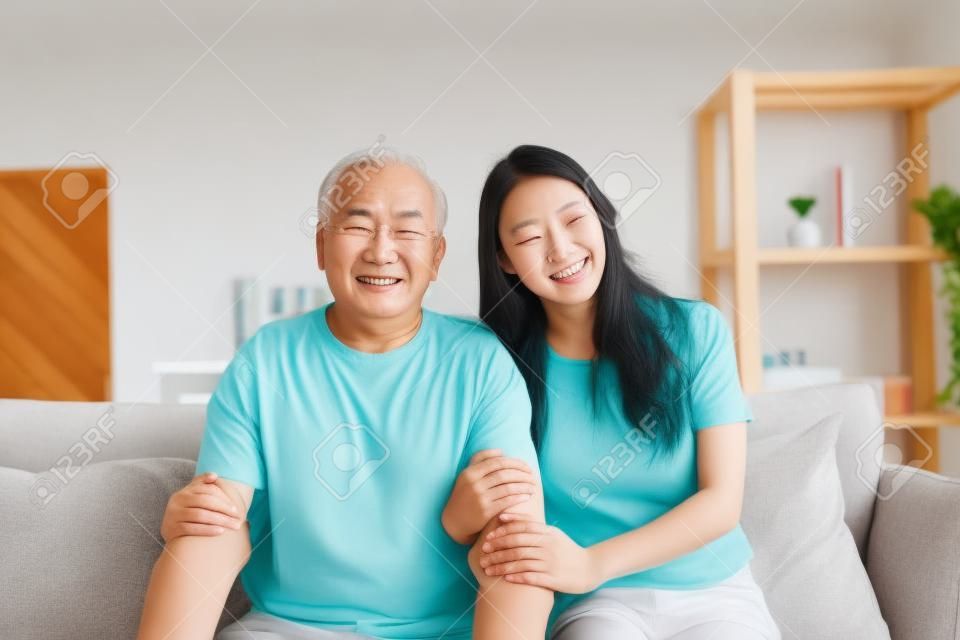 Retrato da filha asiática bonita abraçando e sentar-se com o pai mais velho. Mulher atraente neta visita o homem maduro sênior em casa, aproveite passar o tempo juntos na sala de estar, em seguida, olhando para a câmera