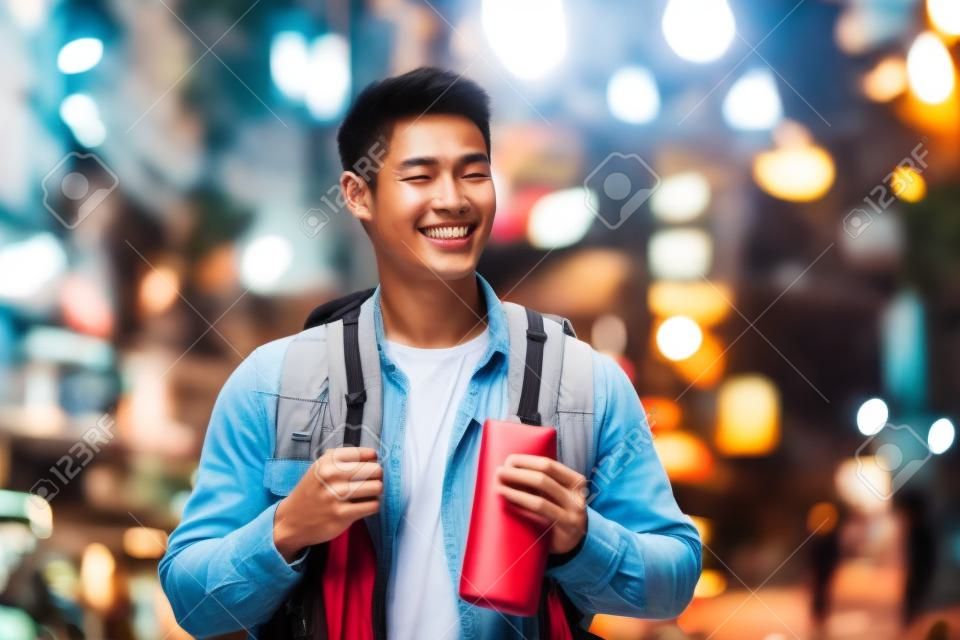 Asian young man backpacker traveler look at map to find destination. Attractive handsome tourist girl travel alone on street, enjoy walking in the city at night on holiday vacation trip in Thailand