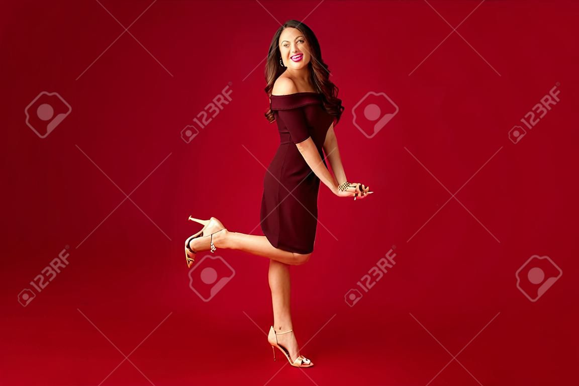 Full lengh portrait of elegant young woman in maroon dress over red background.