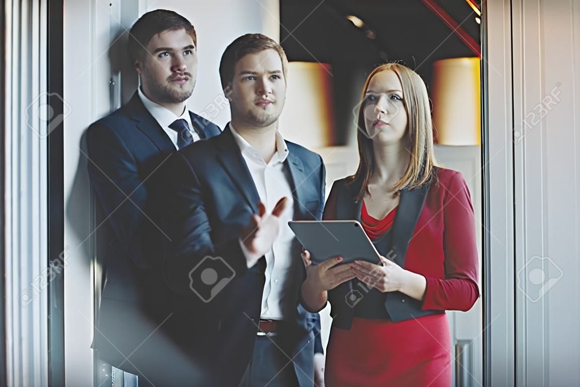 비즈니스 사람들이 그룹 : 공식적인 양복과 빨간 드레스와 자 켓을 들고 재킷에 남자에서 남자 남자 뭔가 창과 열, 사무실 인테리어 사이 서 서 자신의 여성 동료에 보이고있다