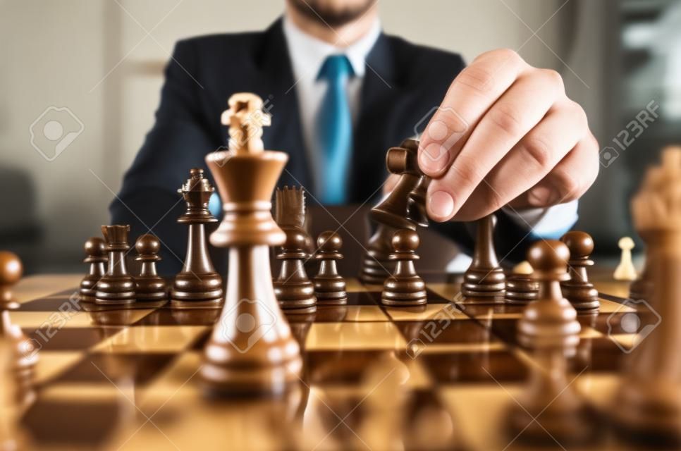 Retro style image of a businessman with clasped hands planning strategy with chess figures on an old wooden table.