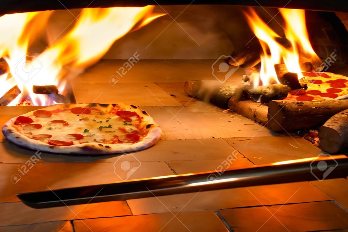 Close up de pizza en horno de leña con llama detrás