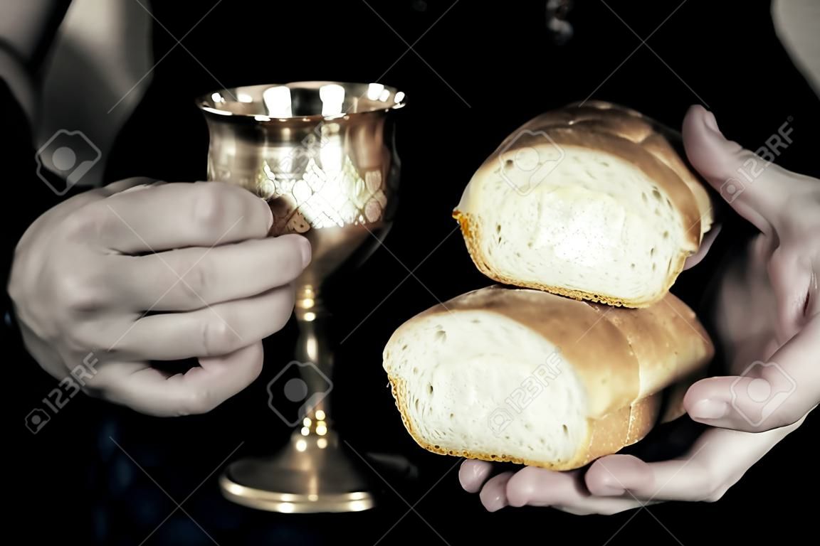 Two hands holding bread and wine for communion, isolated on black