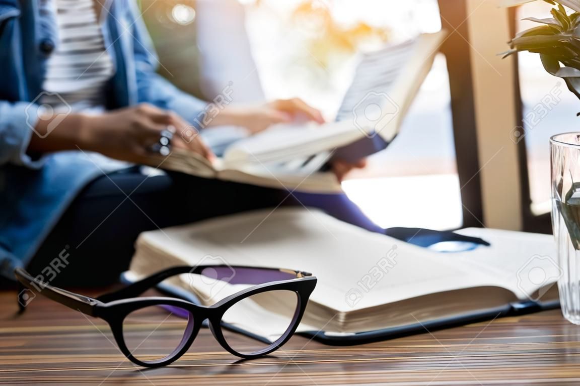 focus at glasses and background of woman sitting in a cafe, reading book.