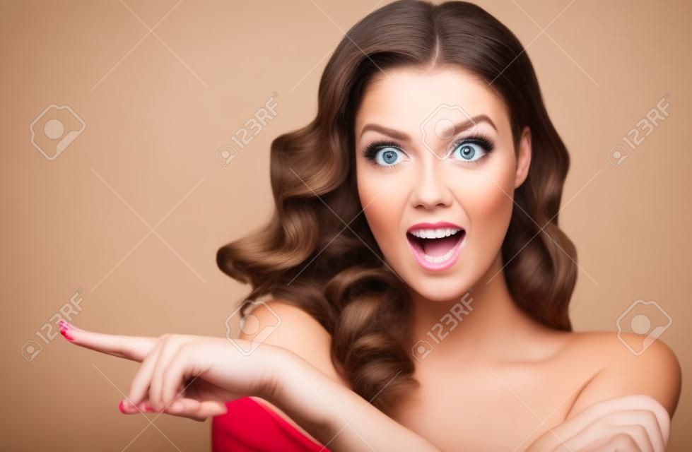 Surprised woman demonstrates invisible product .Beautiful girl with curly hair pointing to the side. Bright facial expression.
