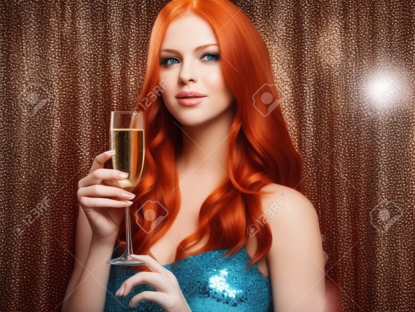 Giovane, splendida donna dai capelli rossi con capelli voluminosi sta tenendo un bicchiere di vino champagne sullo sfondo blu brillante scintillante.