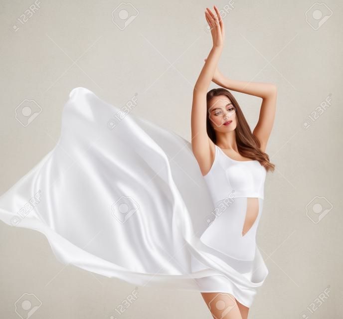 Młoda, ponętna kobieta o wdzięcznym i smukłym ciele, ubrana w białą sportową bieliznę i częściowo pokryta delikatnym, jedwabnym materiałem. Smukła postać kobieca, jako symbol zdrowia i harmonii.