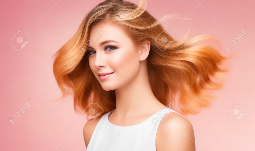 Model z ciemnymi blond włosami. Kręcone, rozwiane włosy okalają śliczną buzię czule uśmiechniętej młodej kobiety. Naturalny połysk i miękkość zdrowych włosów.