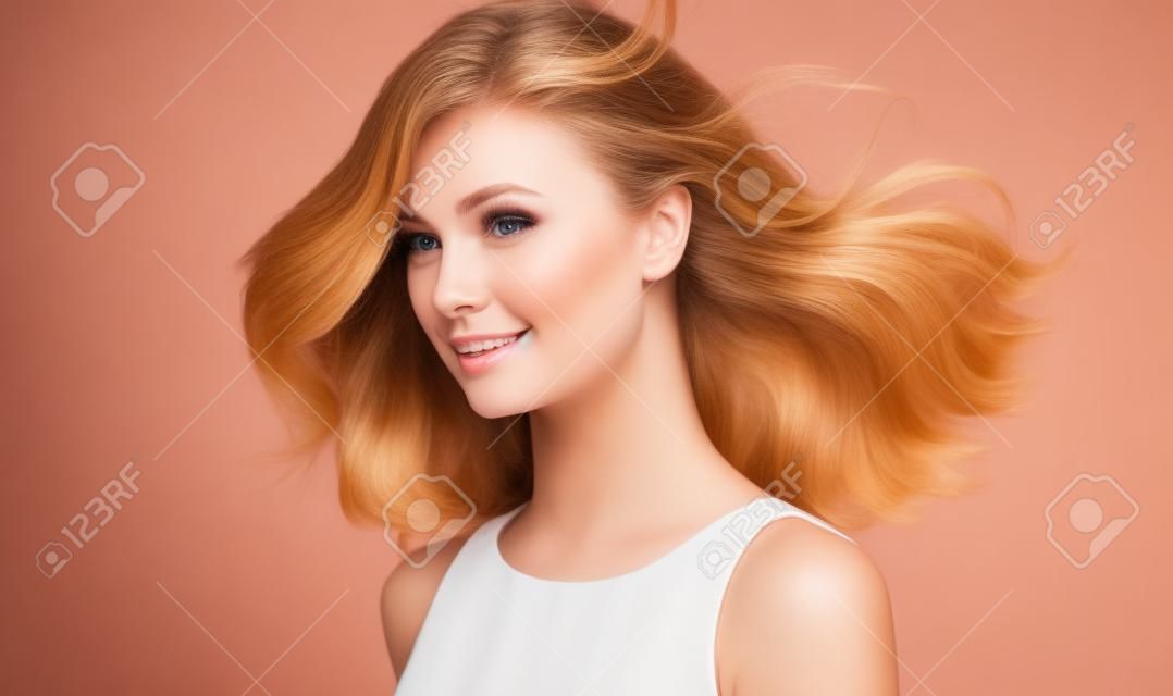 Modelo com cabelo loiro escuro. Frizzy, cabelo voador é em torno de rosto bonito de mulher jovem ternamente sorridente. Gloss natural e suavidade de cabelo saudável.