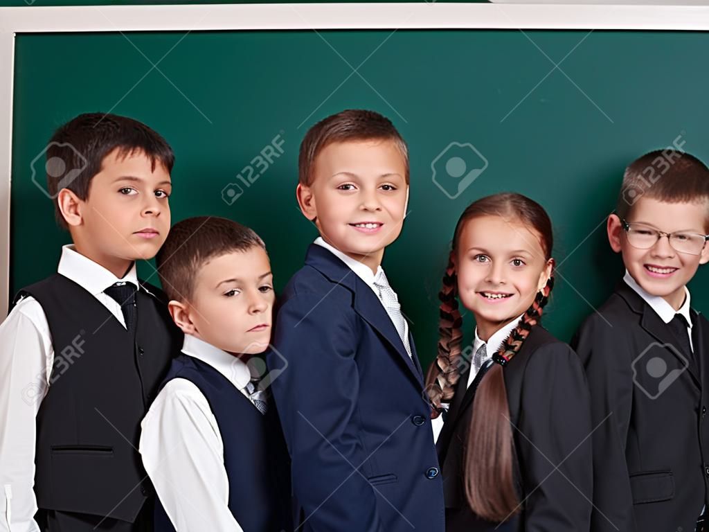 elementary school boy near blank chalkboard background, dressed in classic black suit, group pupil, education concept