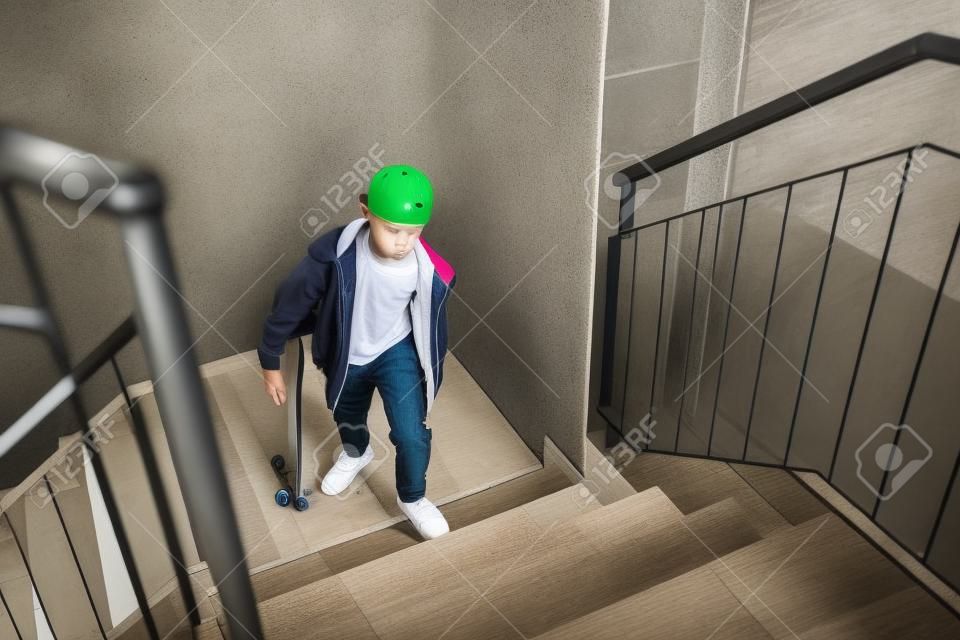 Menino skatista adolescente com um skate subindo por escada em casa.