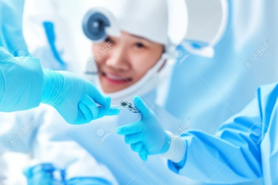 Un team di chirurghi asiatici distribuisce strumenti chirurgici ad altri medici mentre opera pazienti. squadra medica salvavita che detiene attrezzature mediche per salvare la vita dei pazienti. concetto di chirurgia