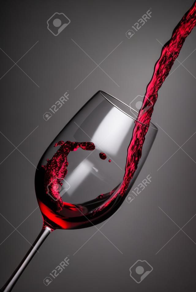 Verter el vino tinto en una copa de cristal y crea olas, salpicaduras vino tinto vertido de la botella en un vaso aislado en fondo blanco