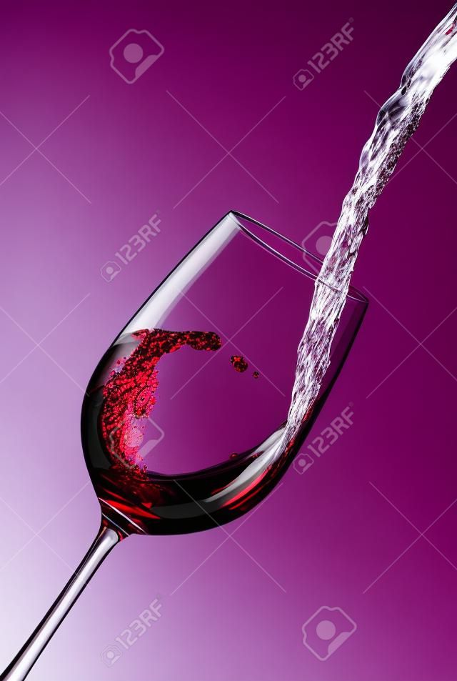 Giet rode wijn in een kristalglas en creëert golven, splash Rode wijn gegoten uit fles in een glas geïsoleerd op witte achtergrond