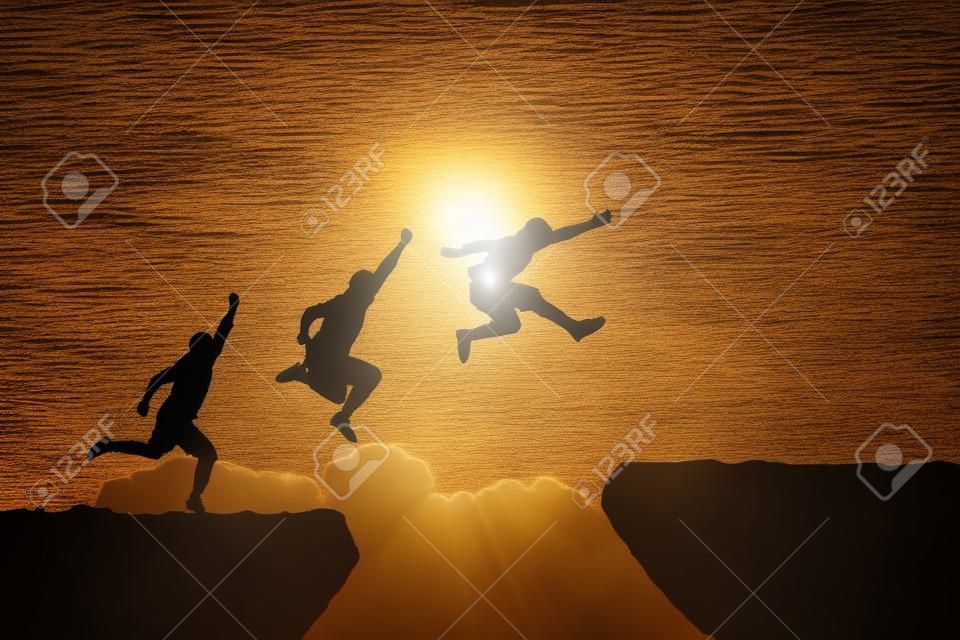 Men jump cliff sun light over silhouette